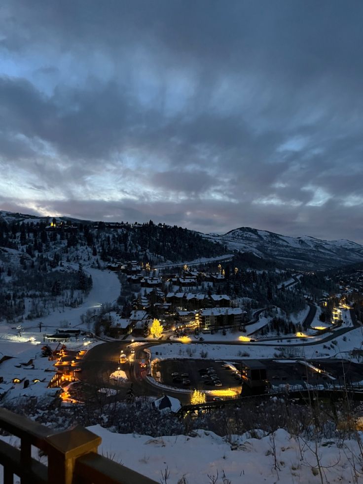 a view of a town at night with snow on the ground and mountains in the background