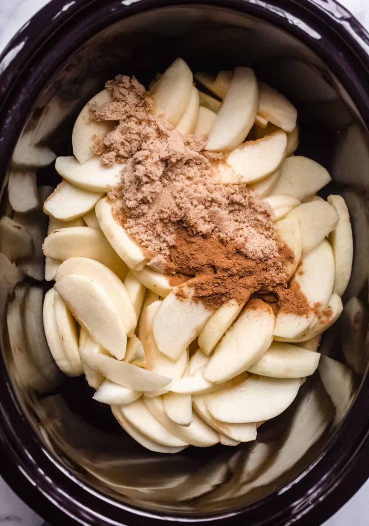 an image of apples in the crock pot with cinnamon and powdered sugar on top