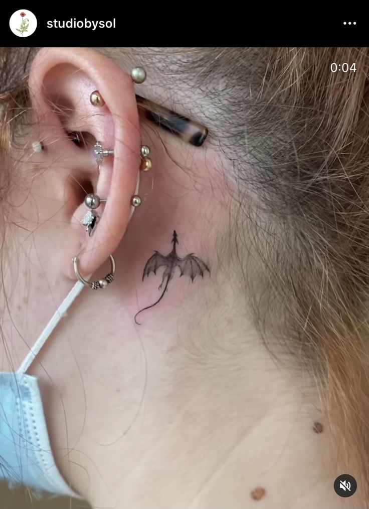 a woman with a dragon tattoo on her ear and behind the ear is a piercing