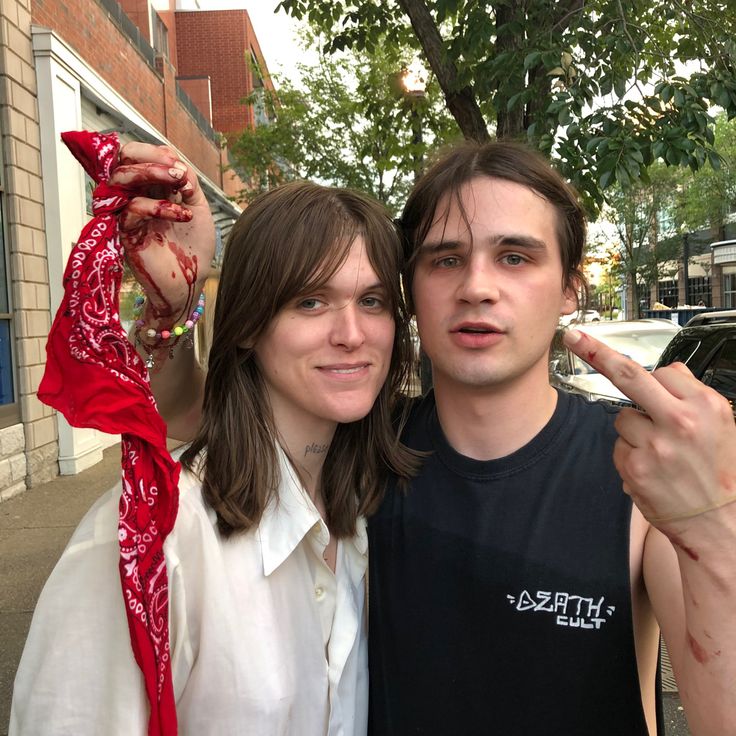 two people standing next to each other in front of a building and one person pointing at the camera