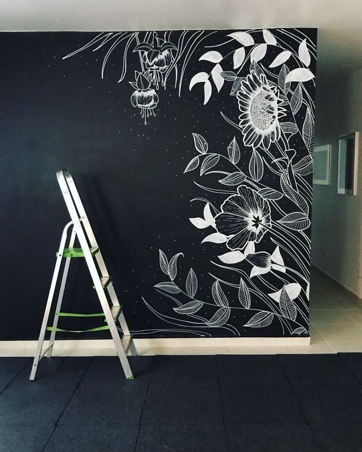 a black wall with white flowers painted on it and a ladder leaning against the wall