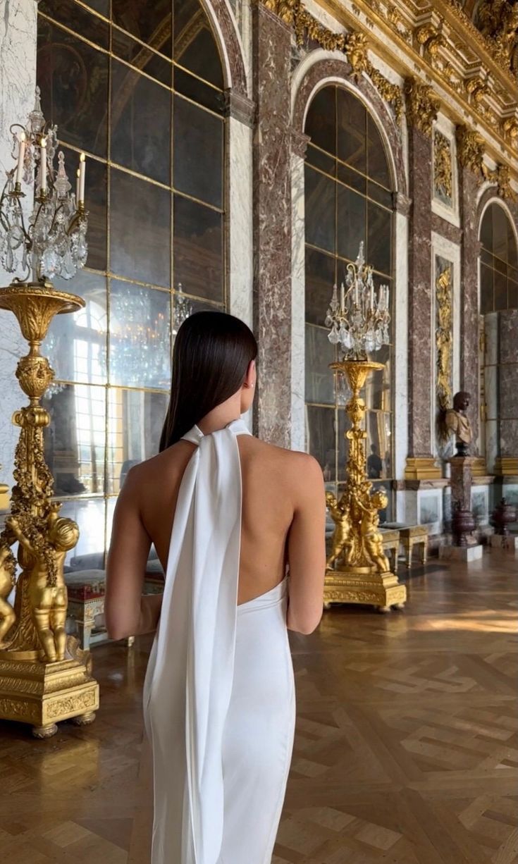 the back of a woman in a white dress looking at chandeliers and mirrors