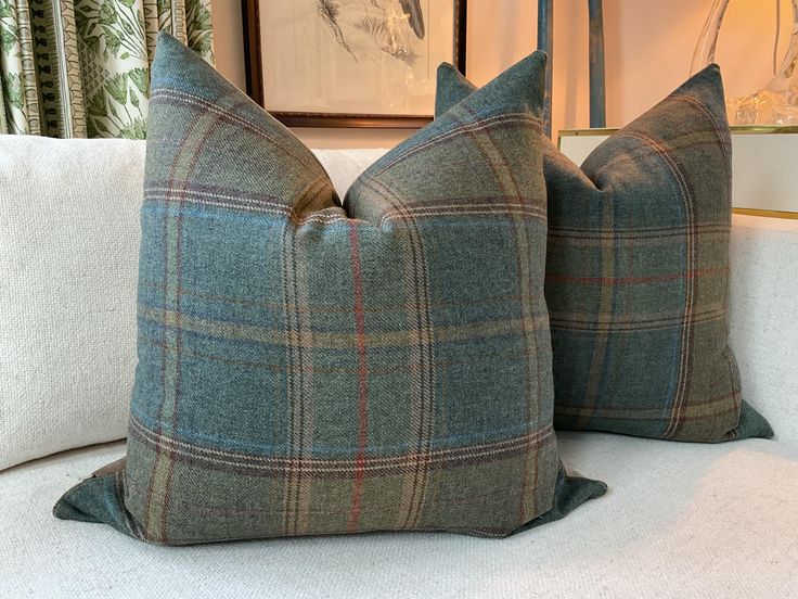 two blue and green plaid pillows sitting on top of a white couch next to a painting