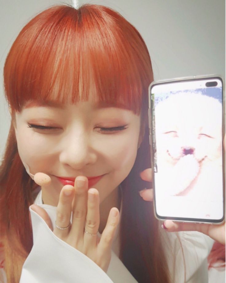 a woman with red hair holding up a cell phone to her face and smiling at the camera