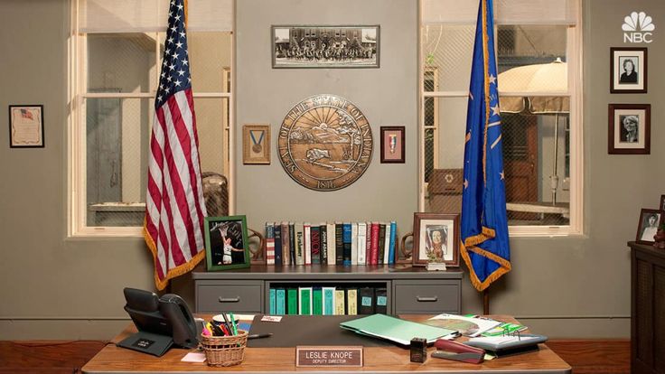 an office with two flags and books on the desk in front of it, along with other items