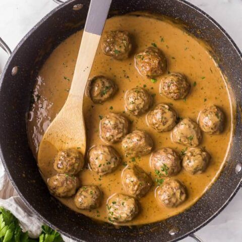 a skillet filled with meatballs and gravy next to a wooden spoon