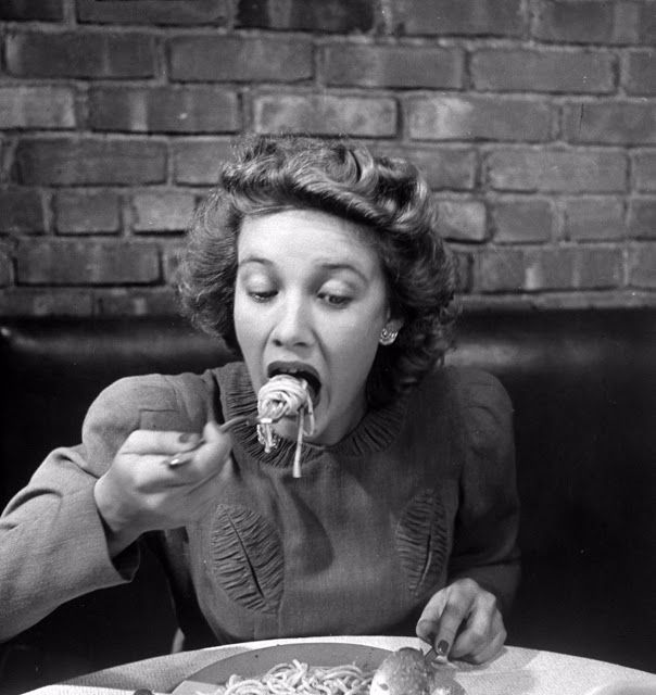 a woman sitting at a table eating spaghetti