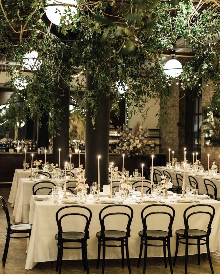 the tables are set with white tablecloths and black chairs, surrounded by greenery