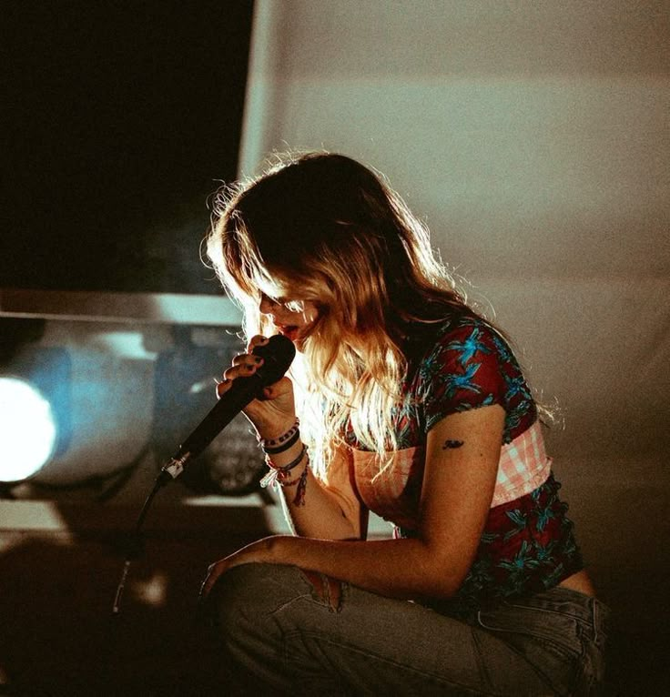 a woman sitting on the ground with a microphone in her hand and she is looking down