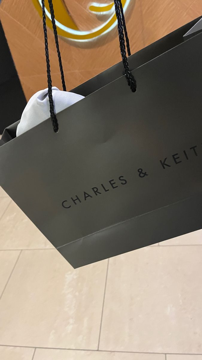 a black shopping bag with the name charles and kitt on it hanging from a ceiling