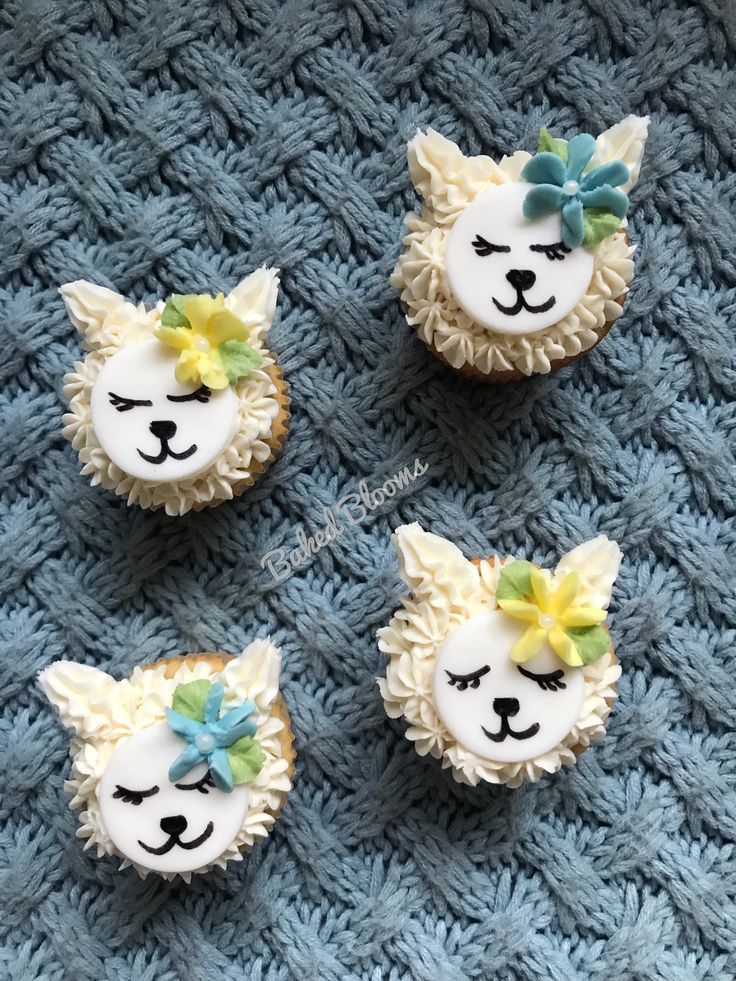 four cupcakes with white frosting and yellow bows on them are sitting on a blue blanket