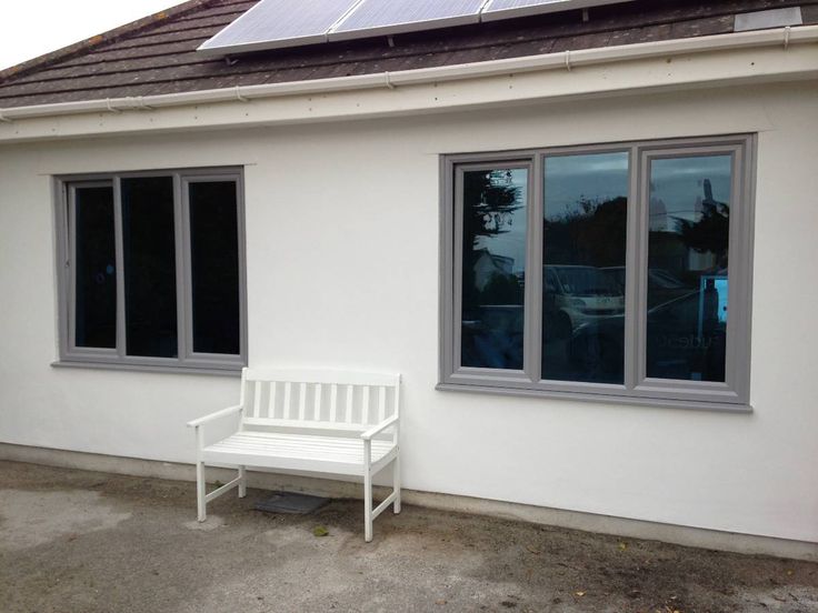 a white bench in front of a house with solar panels on the roof and windows