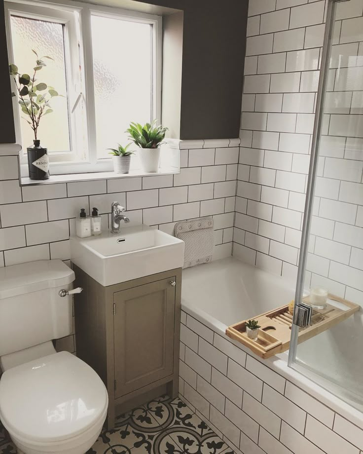 a white toilet sitting next to a bath tub under a bathroom window with a plant in it