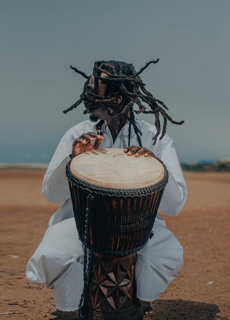 a man with dreadlocks sitting on top of a drum in the desert,