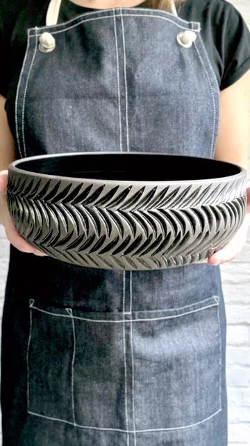 a woman in an apron is holding a large black bowl with silver designs on it