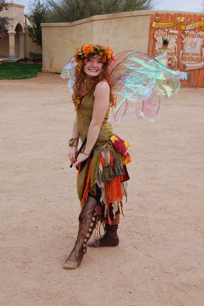 a woman dressed as a fairy with wings and flowers on her head is standing in the sand