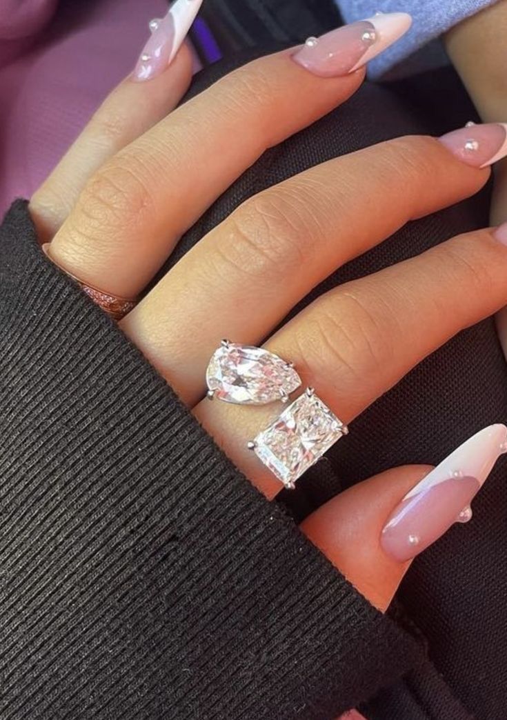 a woman's hand with pink and white nail polish on it, holding an engagement ring