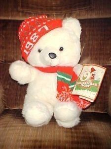 a white teddy bear wearing a red hat and scarf sitting on a chair with a book