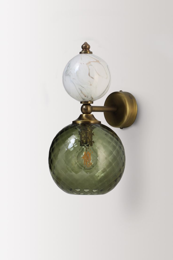 a green glass light fixture mounted on a wall with a white marbled ball hanging from it's side