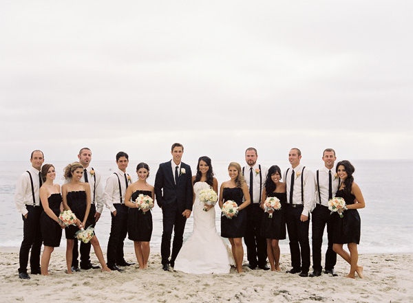 a group of people standing on top of a sandy beach next to the ocean in formal wear