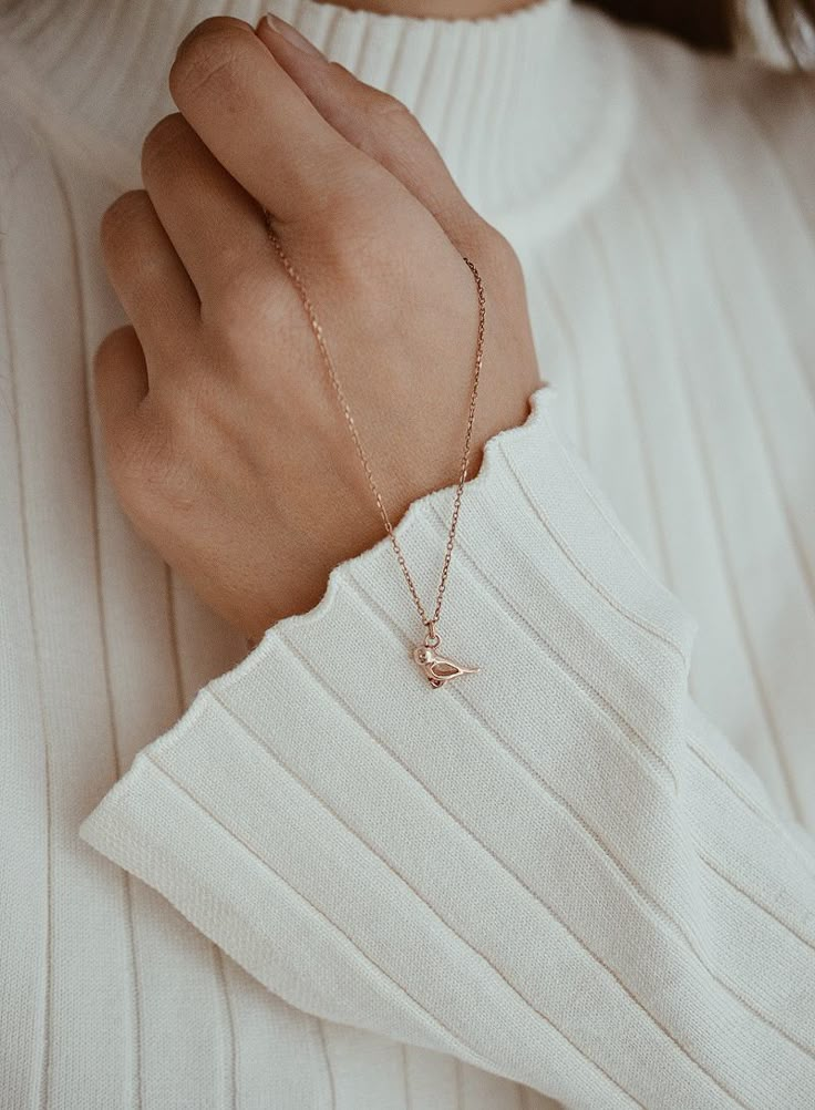 a close up of a person wearing a white sweater and holding a gold bracelet with a small bird on it