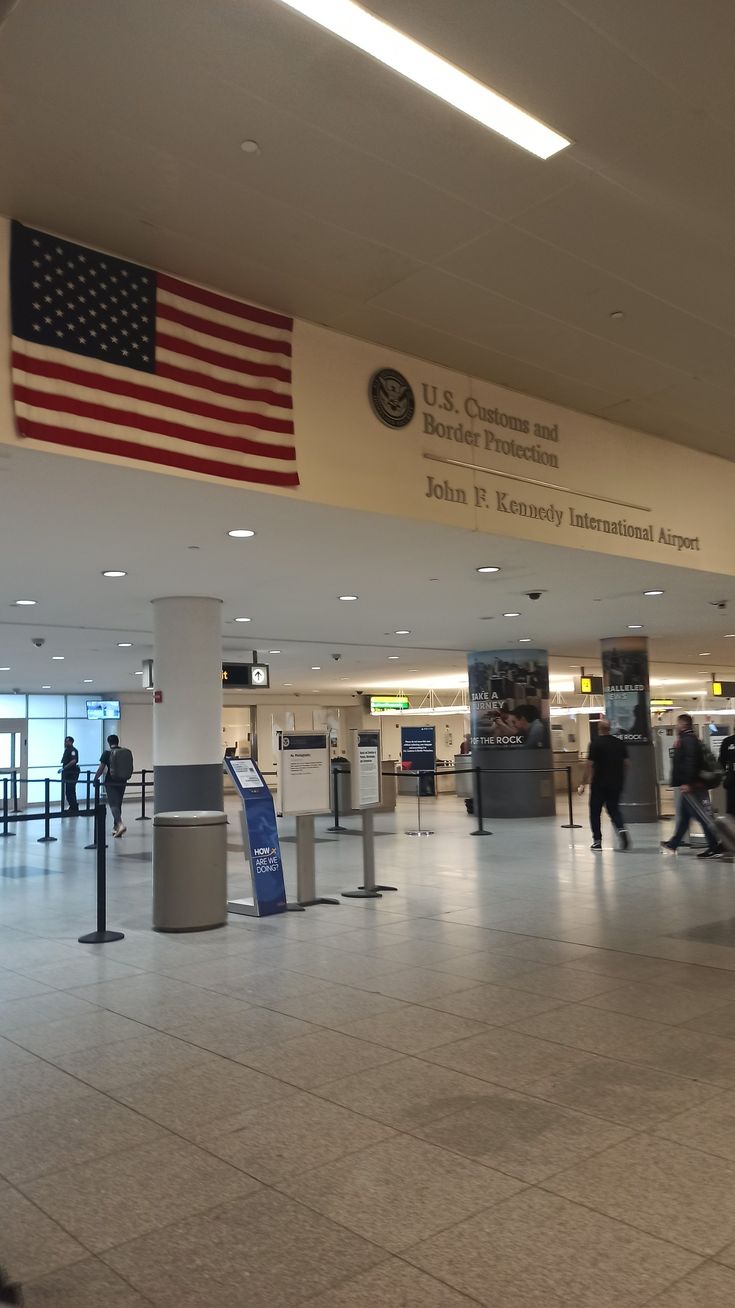 people are walking through an airport terminal with american flags on the wall and luggage carousels