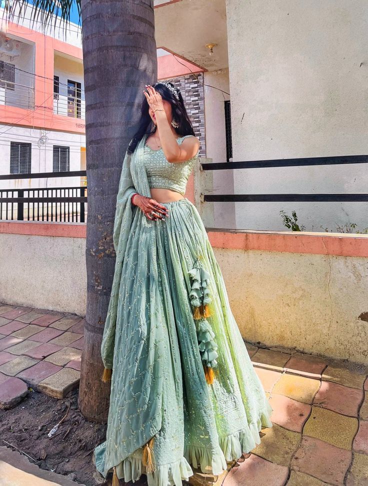 a woman standing next to a palm tree wearing a green and yellow lehenga