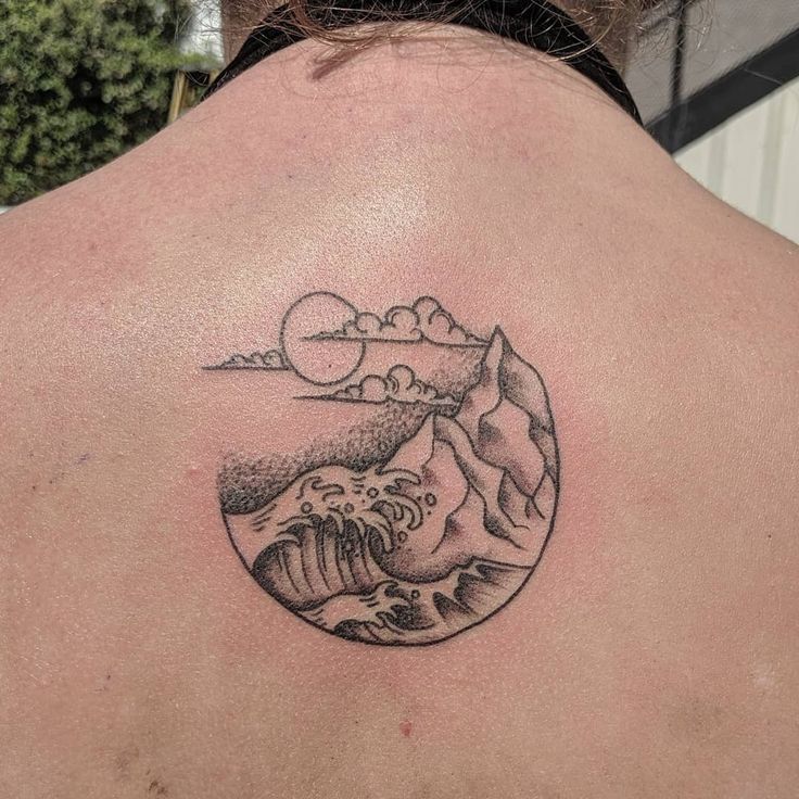 a woman with a tattoo on her back is looking at the ocean and mountains in the distance