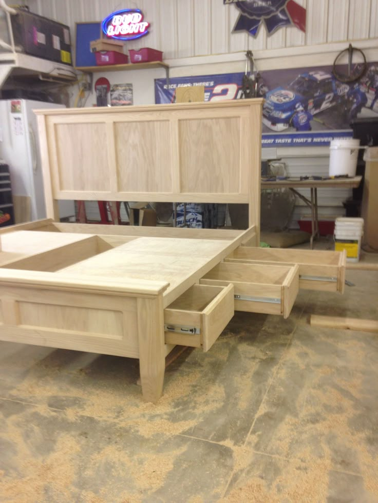 an unfinished bed frame in a garage with drawers on the bottom and side panels open