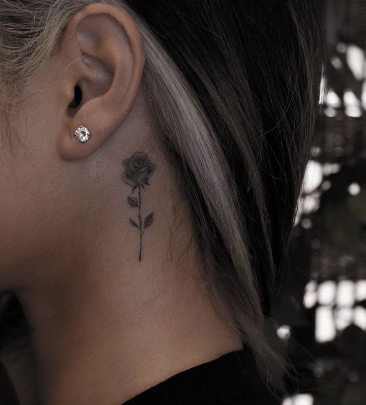 a woman's neck with a small flower tattoo on her left side behind the ear