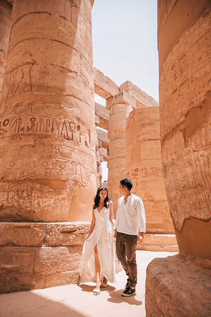 a man and woman standing next to each other in front of some large stone pillars