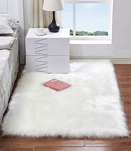 a bedroom with a bed, nightstand and white fur rug on the floor in front of a window