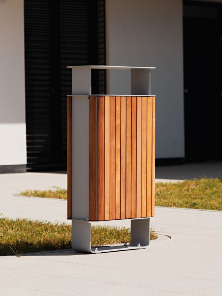 a wooden trash can sitting on the side of a road next to a building and grass