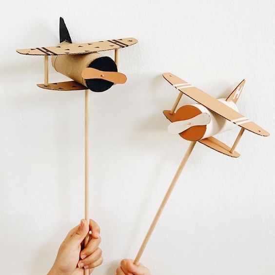 two handmade wooden airplanes on sticks in front of a white wall with one being held by the other