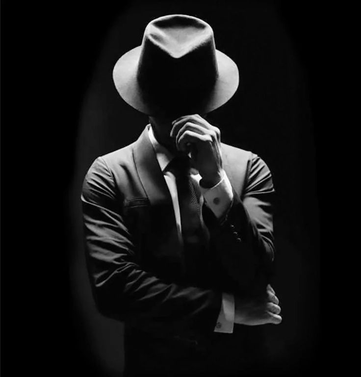 a man in a suit and hat is covering his face with his hands while wearing a fedora