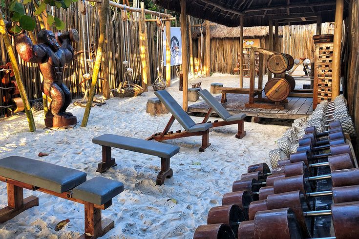 an outdoor area with several benches and chairs in the sand near a fenced in bamboo structure