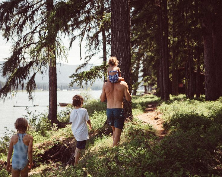 a man and two children are walking in the woods by the water on a sunny day