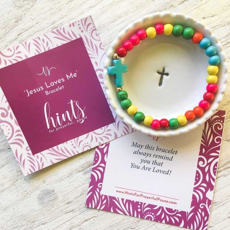 a bowl with candy beads and a cross on it next to a card that says jesus loves me