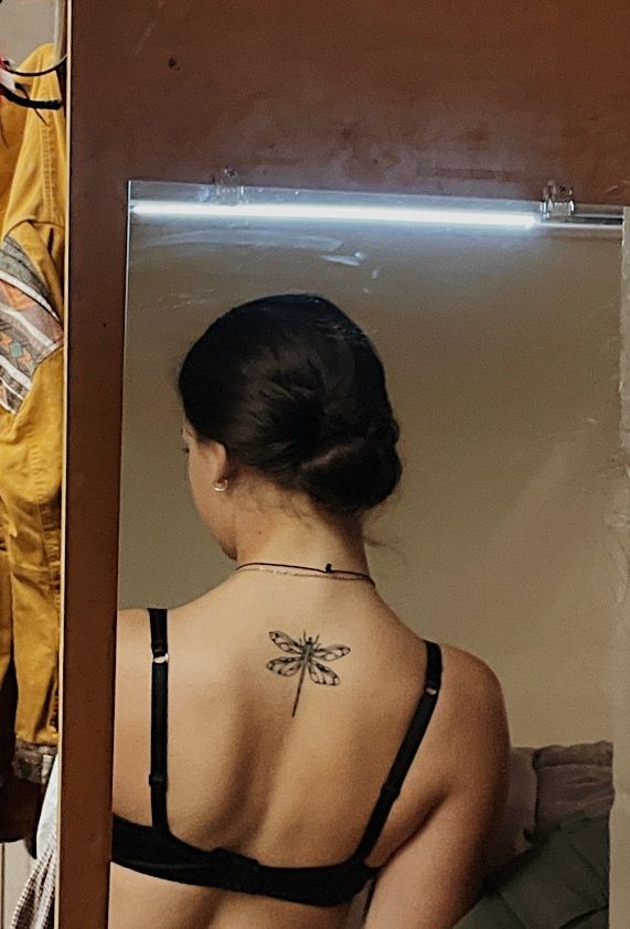 a woman with a tattoo on her back looking at herself in the mirror and wearing a bra