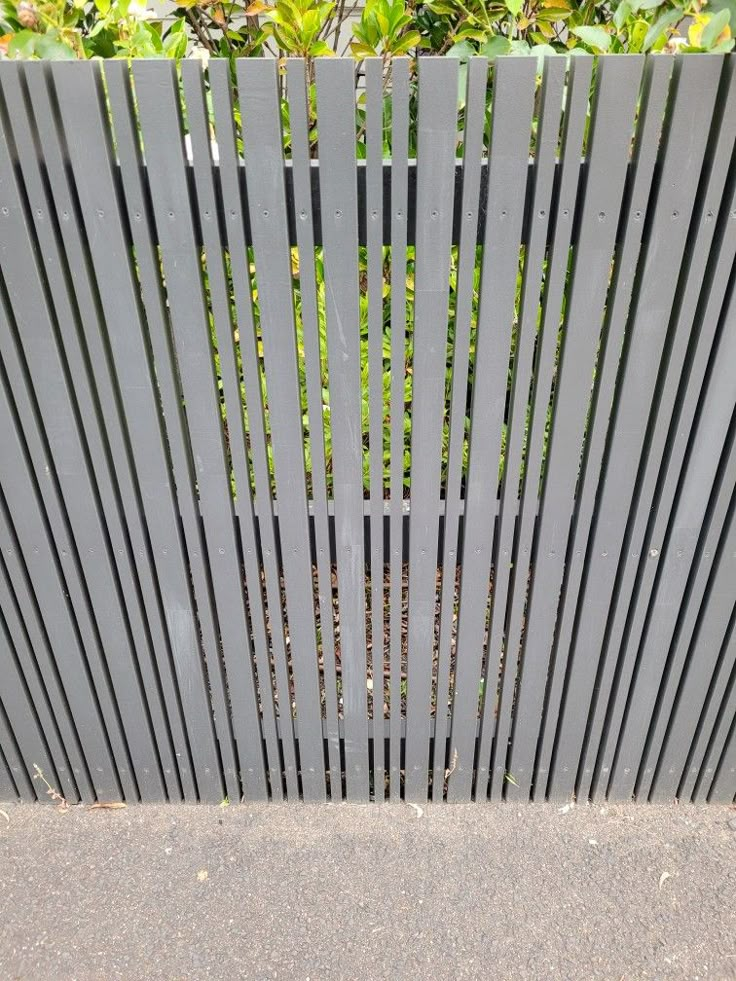 a black fence with vertical slats on the top and bottom, in front of some bushes