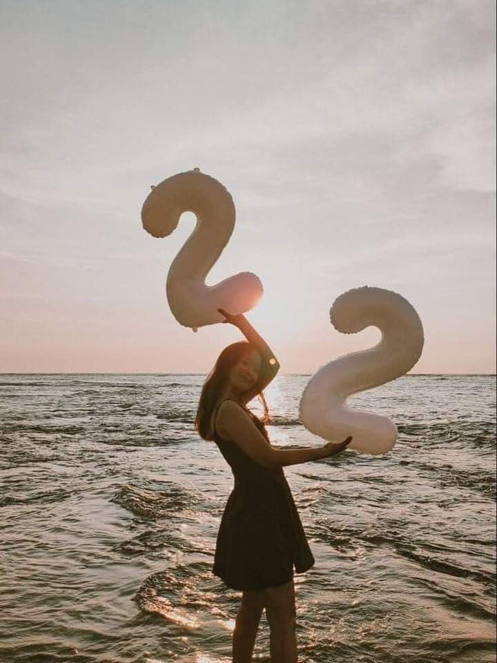 a woman standing in the water holding up two large white balloons that spell out the letter s