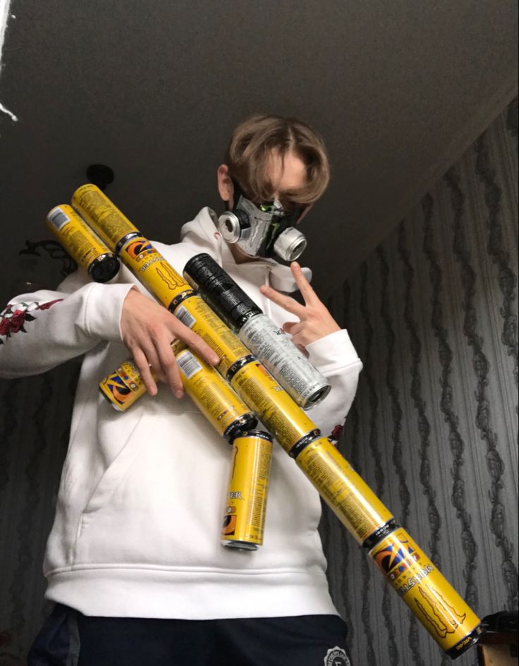 a man in a white hoodie holding yellow and black cylinders with gas masks on them