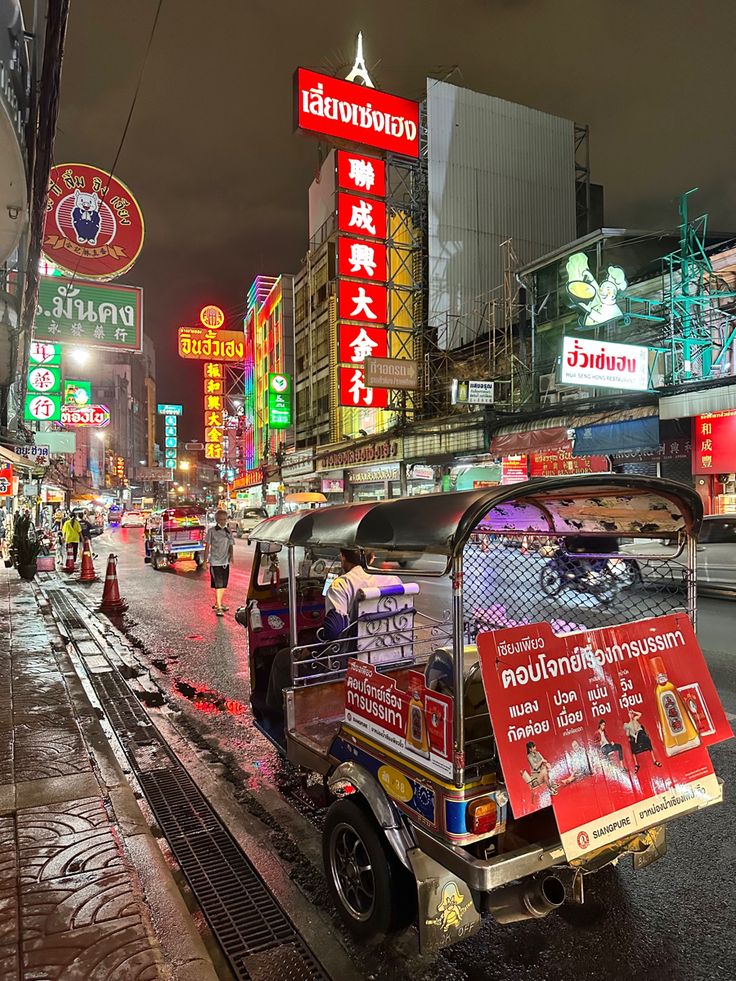 an auto rickshaw is parked on the side of the road in front of neon signs