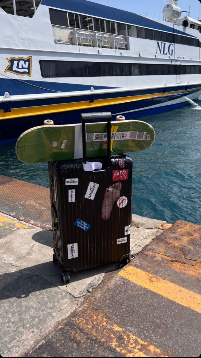 a piece of luggage sitting on top of a sidewalk next to a boat in the water