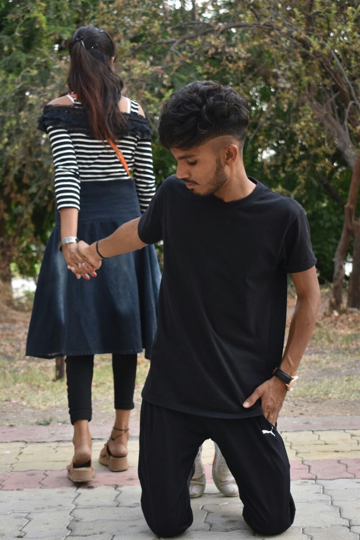 a man standing next to a woman on top of a brick walkway with trees in the background