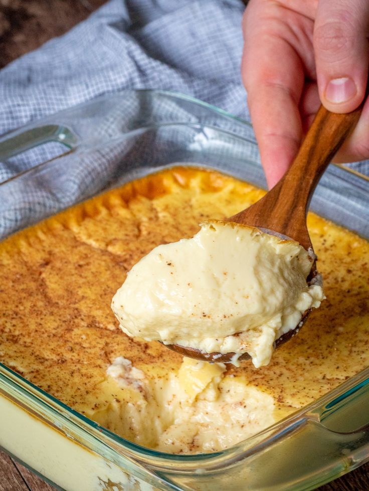 a person scooping mashed potatoes into a casserole dish with a wooden spoon