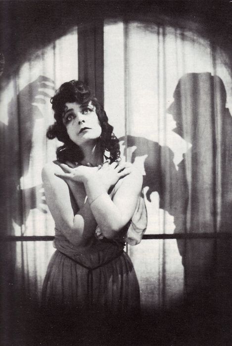 an old photo of a woman standing in front of a window with her hands on her chest