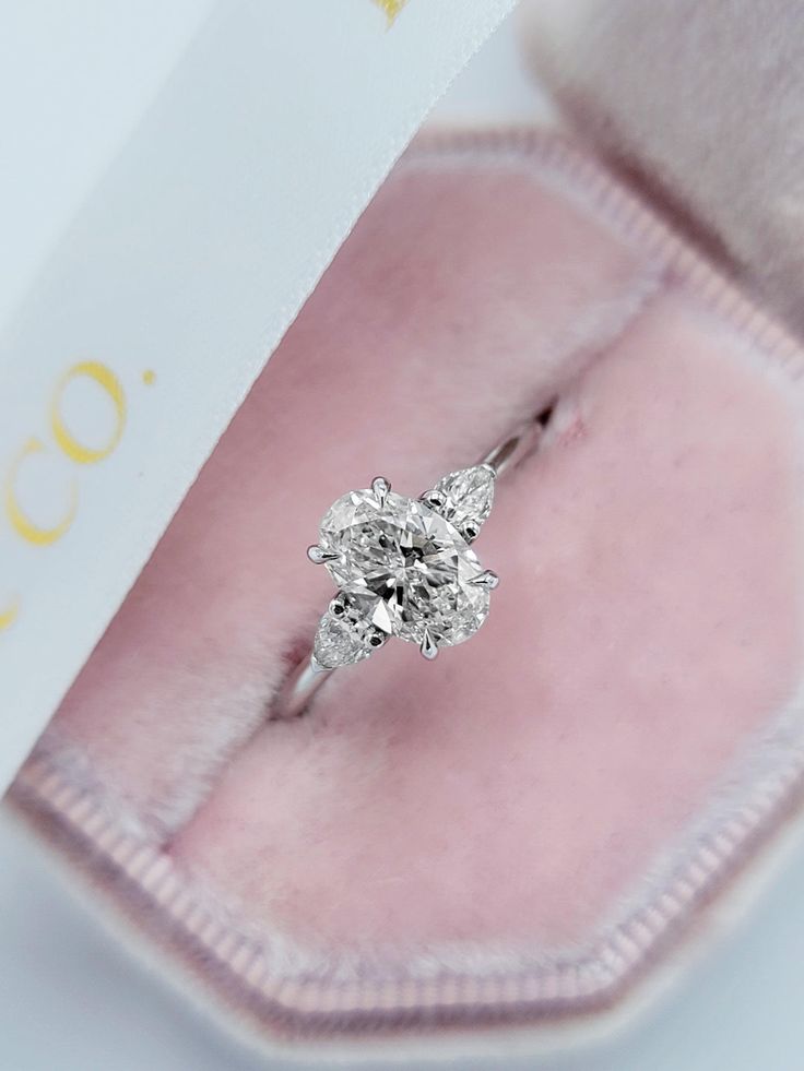 a close up of a diamond ring in a pink velvet box with a tag on it