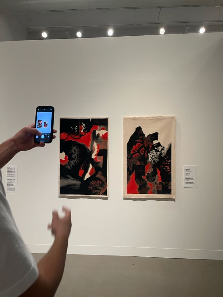 a person holding up a cell phone in front of paintings