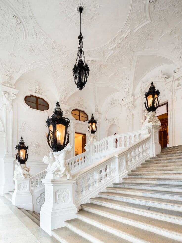 an ornate white staircase with chandeliers and lanterns on the ceiling, along with marble steps